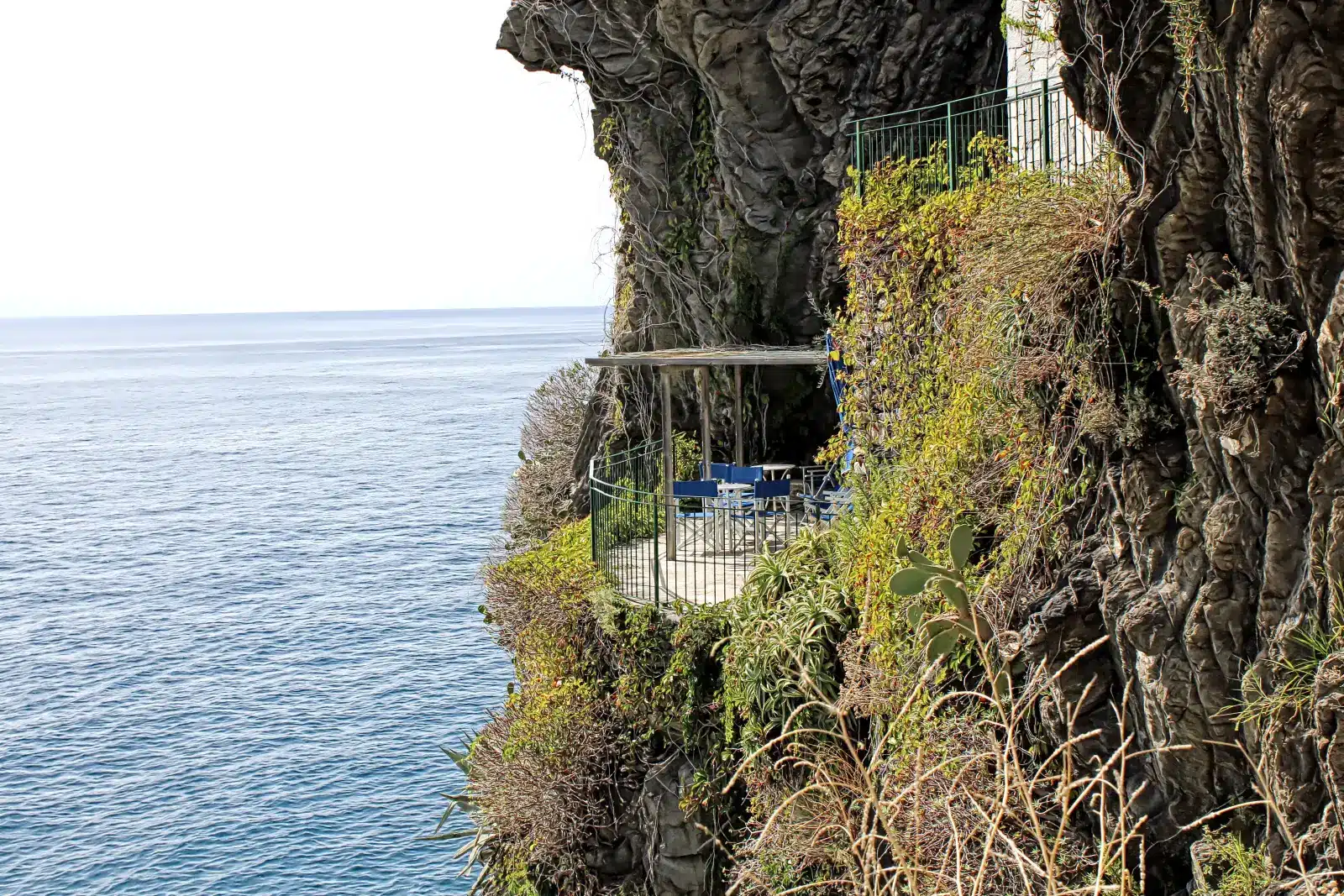 Private blue terrace seating on a steep cliffside balcony overlooking the Ligurian Sea in Cinque Terre, Italy.