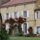 Traditional Périgord golden stone house with climbing roses and white shutters in a historic village of Dordogne, France.