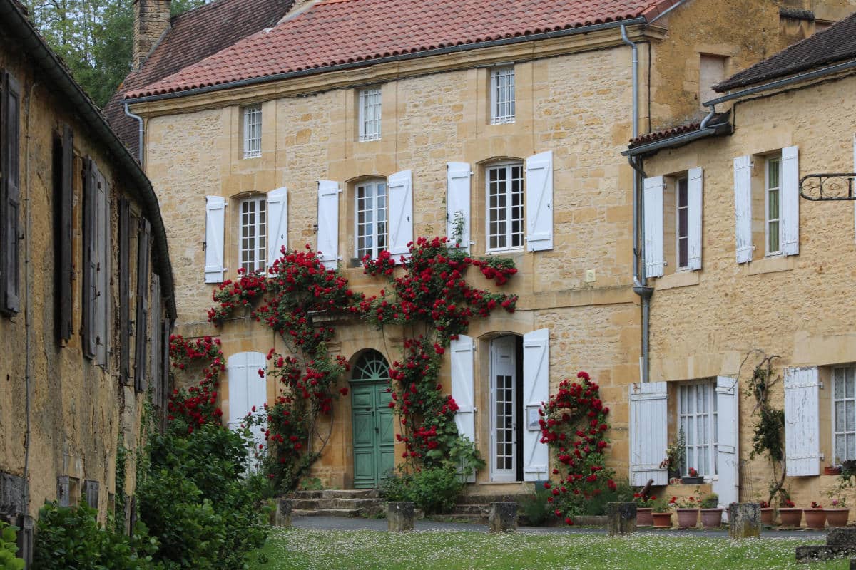 Traditional Périgord golden stone house with climbing roses and white shutters in a historic village of Dordogne, France.