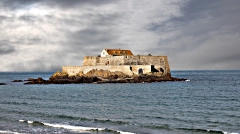 The historic Fort National on its rocky islet in Saint-Malo, surrounded by the sea under a dramatic stormy sky.