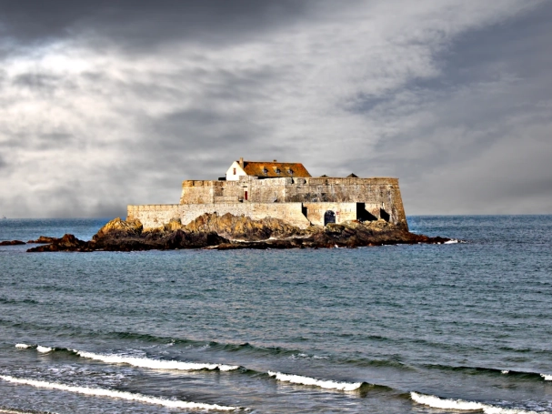The historic Fort National on its rocky islet in Saint-Malo, surrounded by the sea under a dramatic stormy sky.