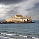 The historic Fort National on its rocky islet in Saint-Malo, surrounded by the sea under a dramatic stormy sky.