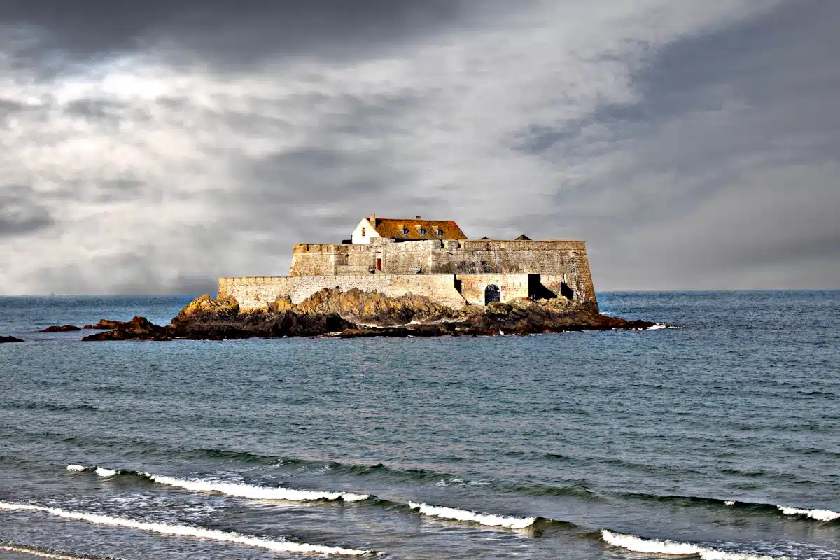 The historic Fort National on its rocky islet in Saint-Malo, surrounded by the sea under a dramatic stormy sky.