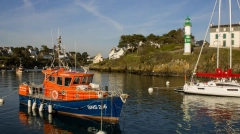 Rescue boat SNS 206 moored in a scenic harbor with a lighthouse and coastal houses in the background