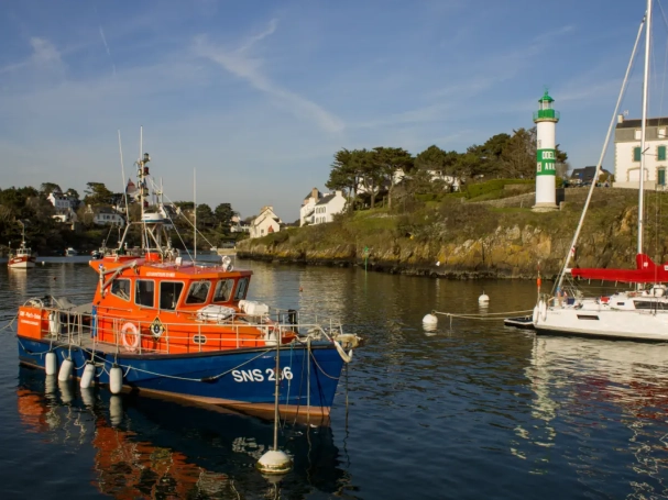 Rescue boat SNS 206 moored in a scenic harbor with a lighthouse and coastal houses in the background