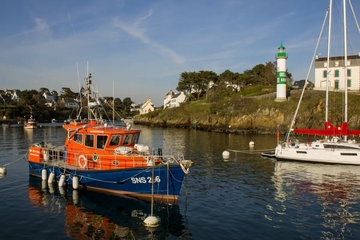Rescue boat SNS 206 moored in a scenic harbor with a lighthouse and coastal houses in the background