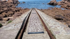 Lifeboat launch ramp with rusty rails leading into the sea, surrounded by pink granite rocks in Ploumanac'h, Brittany.