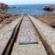 Lifeboat launch ramp with rusty rails leading into the sea, surrounded by pink granite rocks in Ploumanac'h, Brittany.