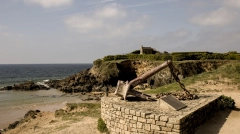 A large rusted memorial anchor at Le Pouldu, Brittany, with the historic customs house on the cliff overlooking the Atlantic coast