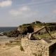 A large rusted memorial anchor at Le Pouldu, Brittany, with the historic customs house on the cliff overlooking the Atlantic coast