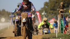 Close-up of a muddy motocross rider leading a pack of competitors on a dirt track."