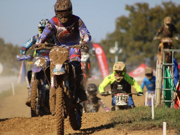 Close-up of a muddy motocross rider leading a pack of competitors on a dirt track."