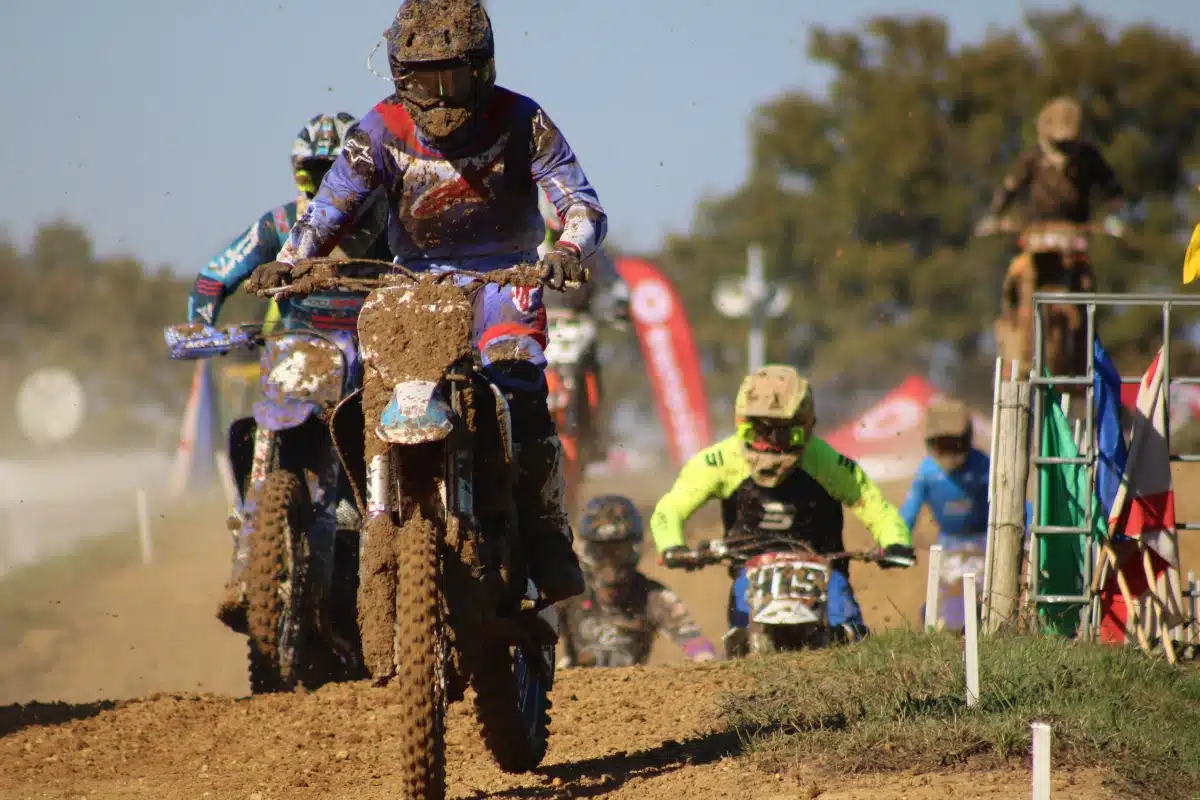 Close-up of a muddy motocross rider leading a pack of competitors on a dirt track."