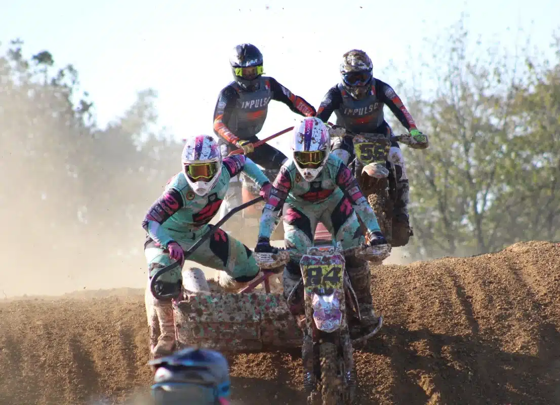 Front view of two sidecarcross teams racing head-to-head on a dusty dirt track