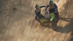 Sidecarcross team leaning hard during a steep downhill descent on a sandy track with backlight dust