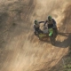 Sidecarcross team leaning hard during a steep downhill descent on a sandy track with backlight dust